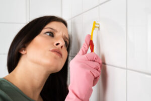 Close-up Of Person Hand Cleaning The Dirty White Tile Of The Wall Using Brush