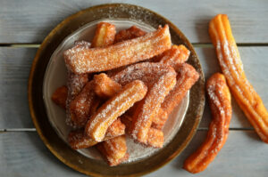 Churros,Sprinkled,With,Powdered,Sugar,On,A,Plate,On,A